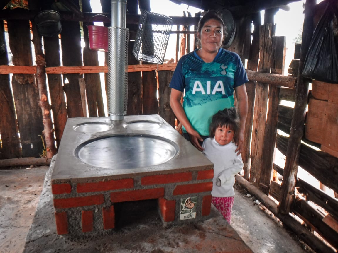 A woman and her child standing in their home next to their Patsari stove.