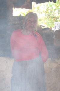 A woman stands in her home surrounded by smoke from her cooking fire.