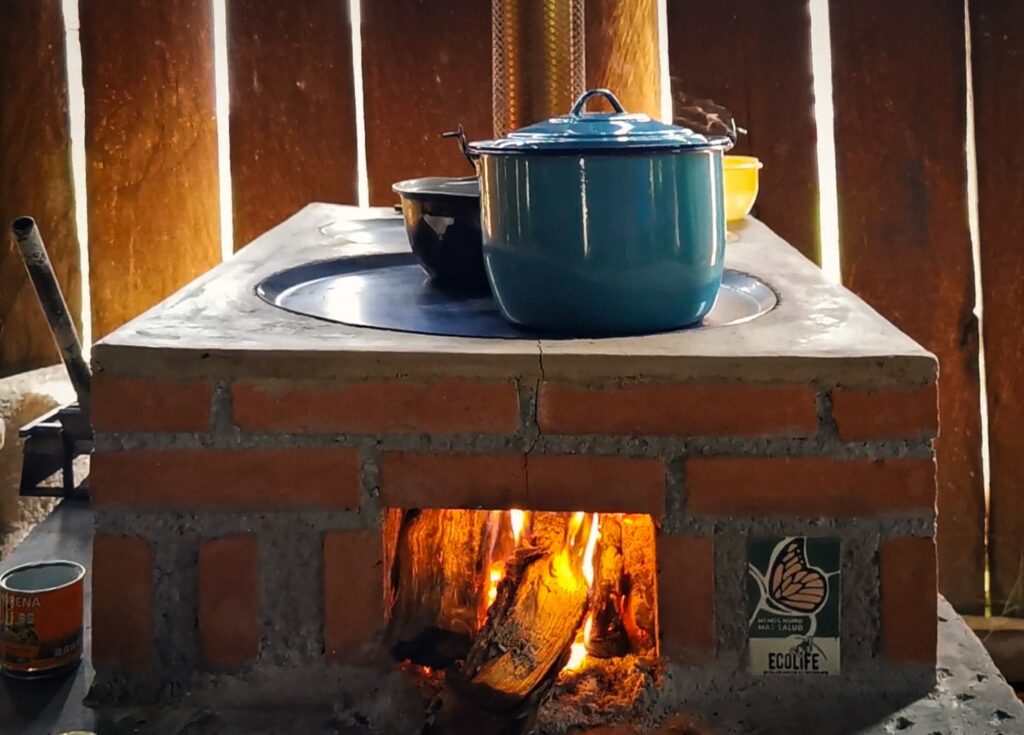 Front view of ECOLIFE's Patsari stove is use with a blue and black pot set on top. The fire powering the stove is visible through a small opening.
